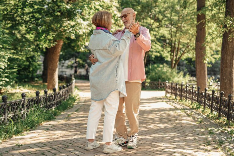 A joyful elderly couple dancing outdoors, showcasing love and happiness in a sunlit park.