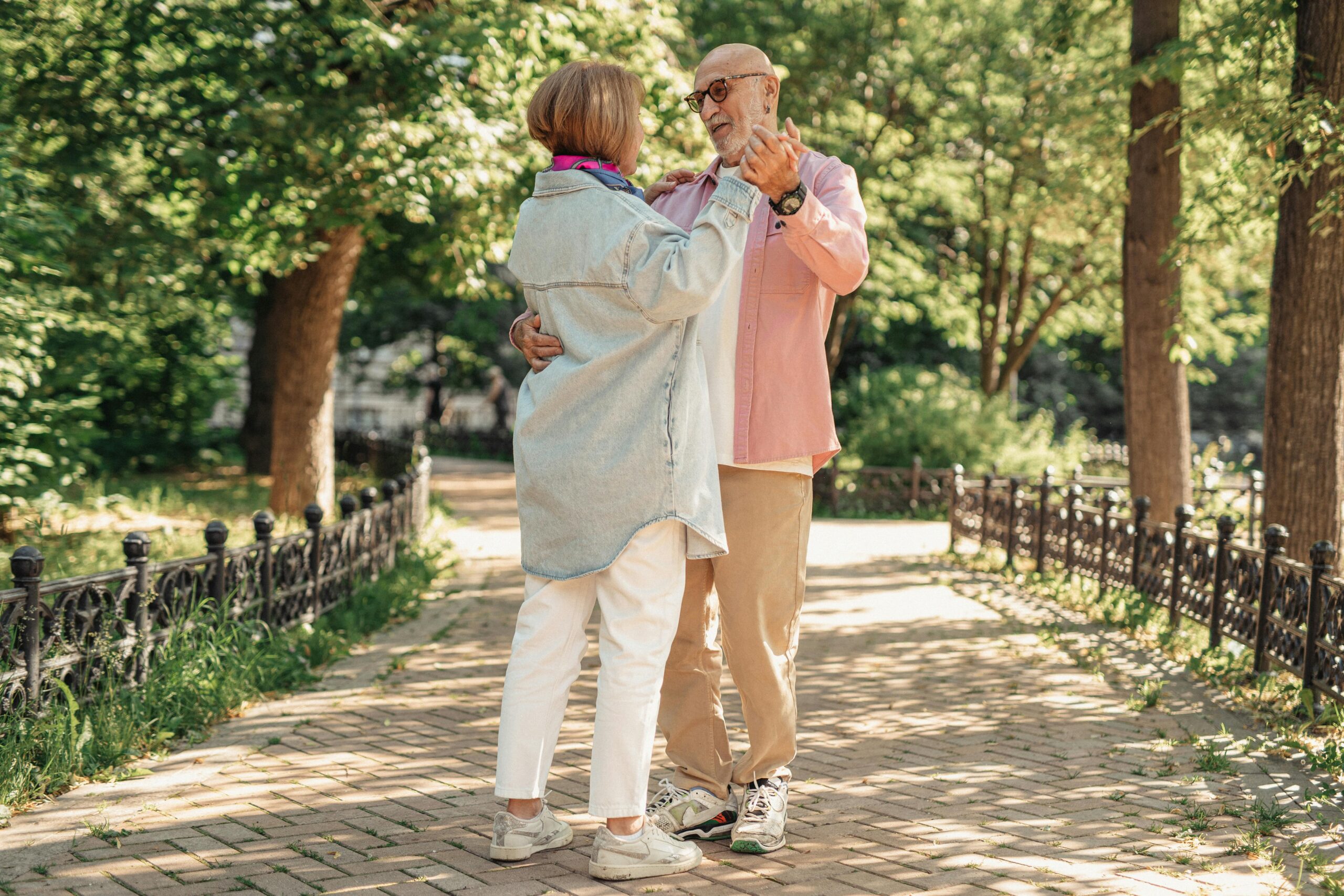 A joyful elderly couple dancing outdoors, showcasing love and happiness in a sunlit park.